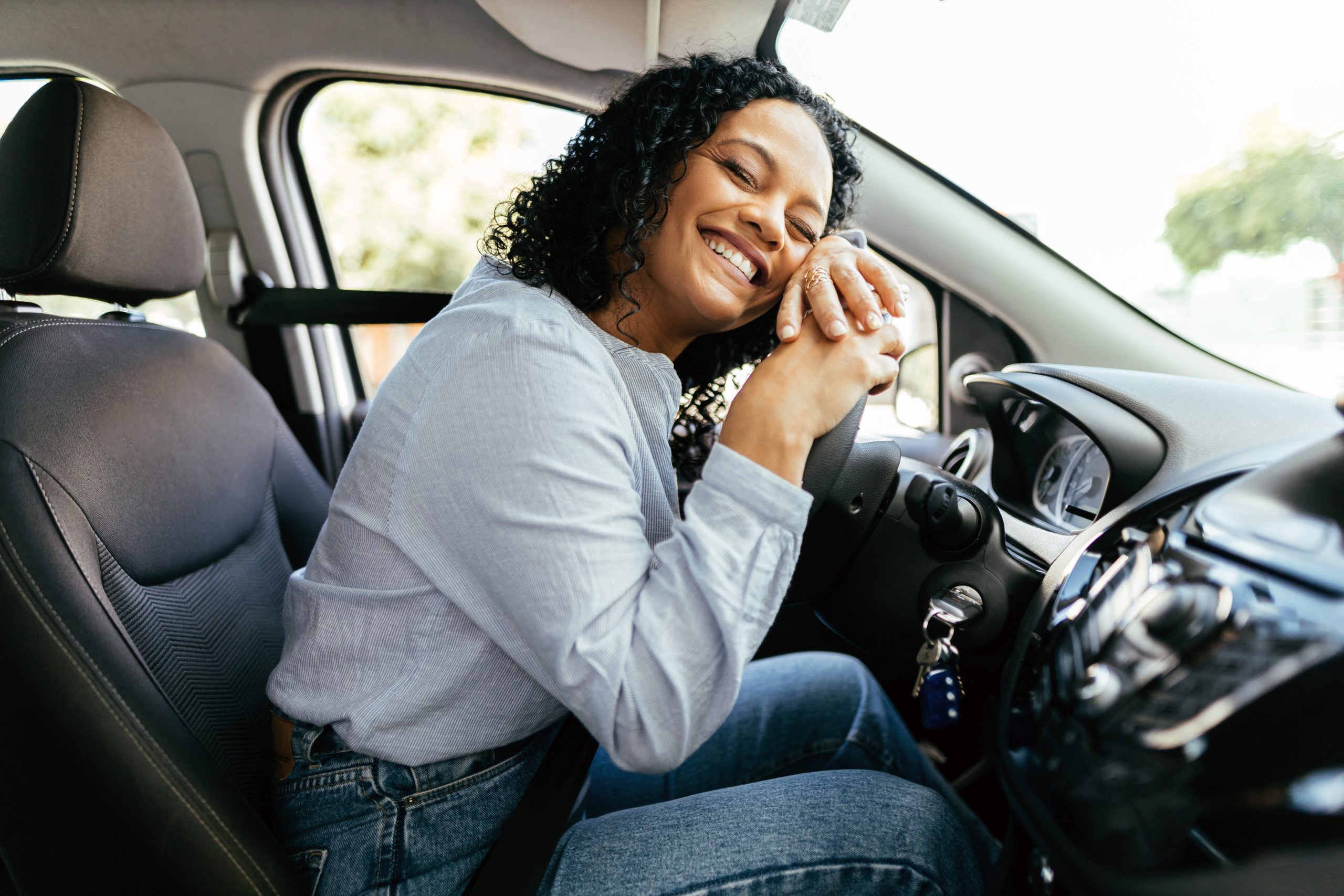 Young and cheerful woman enjoying new car hugging steering wheel sitting inside. Woman driving a new car.